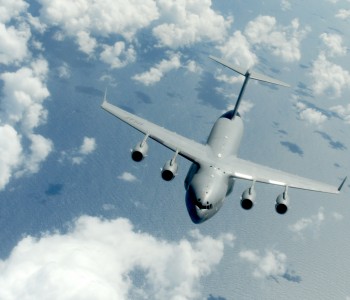 Image of a C-17flying through a cloudy blue sky, returning to Stewart ANGB