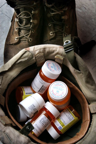 image of prescription pill bottles inside a military helmet next to military boots implying a problem with substance abuse in the military