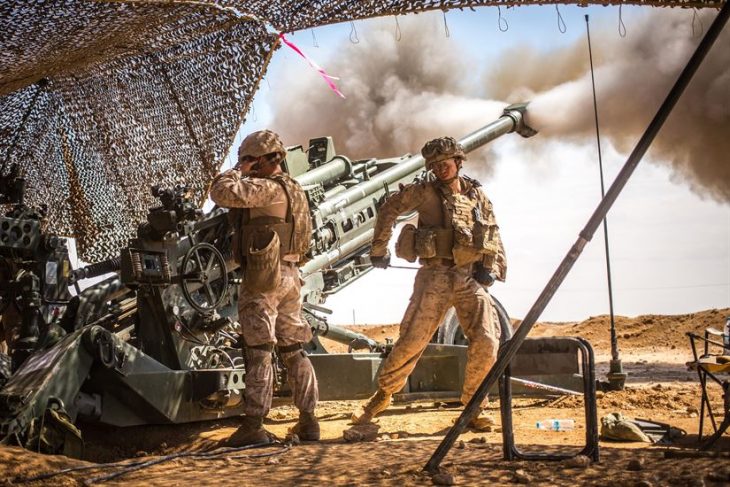 Image of US Army soldiers shooting artillery from under a camouflage net.