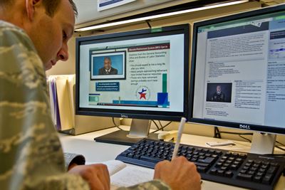 A military member sitting at a desk in front of a computer
